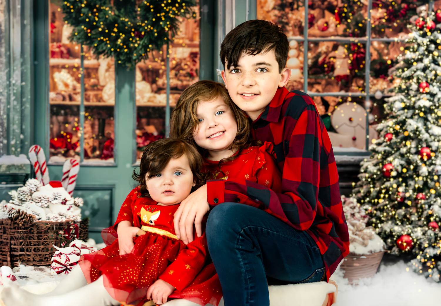 Family wearing red and plaid outfits poses together against a festive Christmas backdrop with twinkling lights.