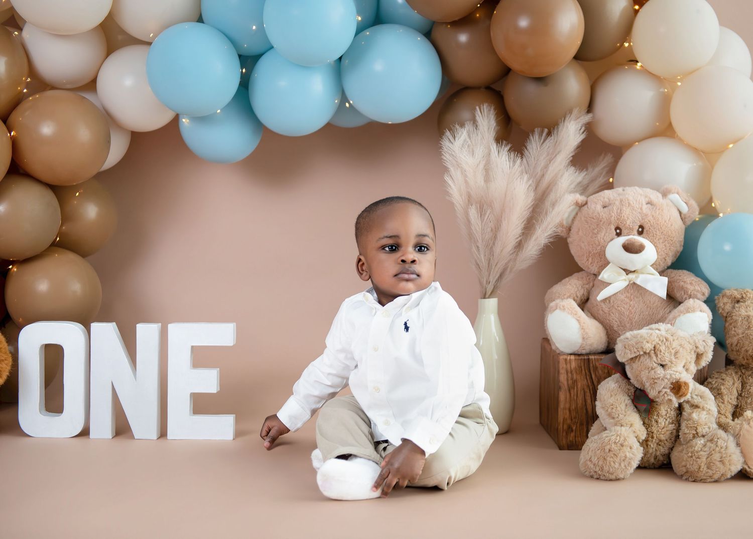 Beige and blue balloon arch with teddy bears and 'ONE' text for a first birthday party decoration setup.