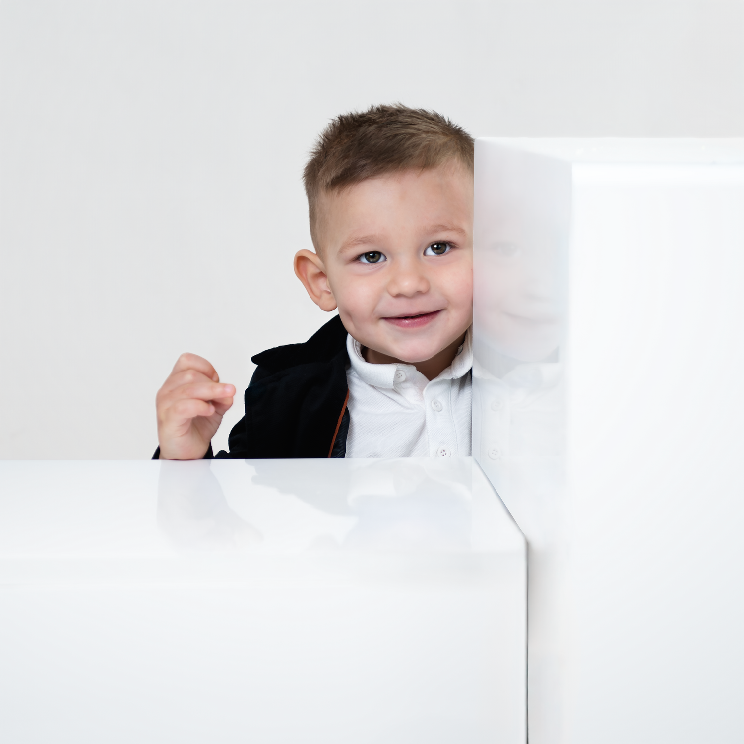 Child in white shirt and black bow tie peeks out playfully from behind white surfaces in three similar photos.