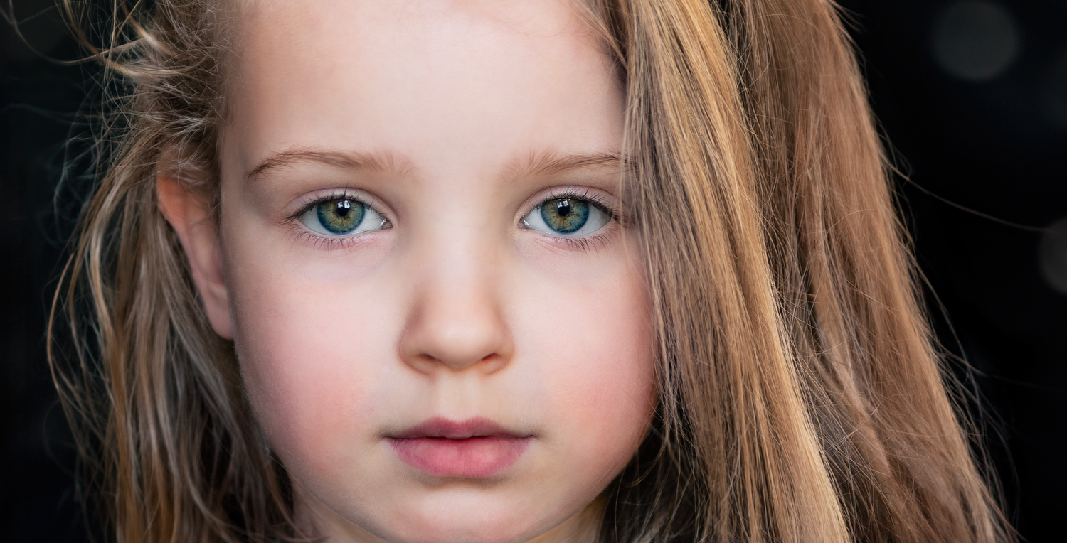 Close up portrait highlighting striking blue eyes and honey blonde hair against a dark background.