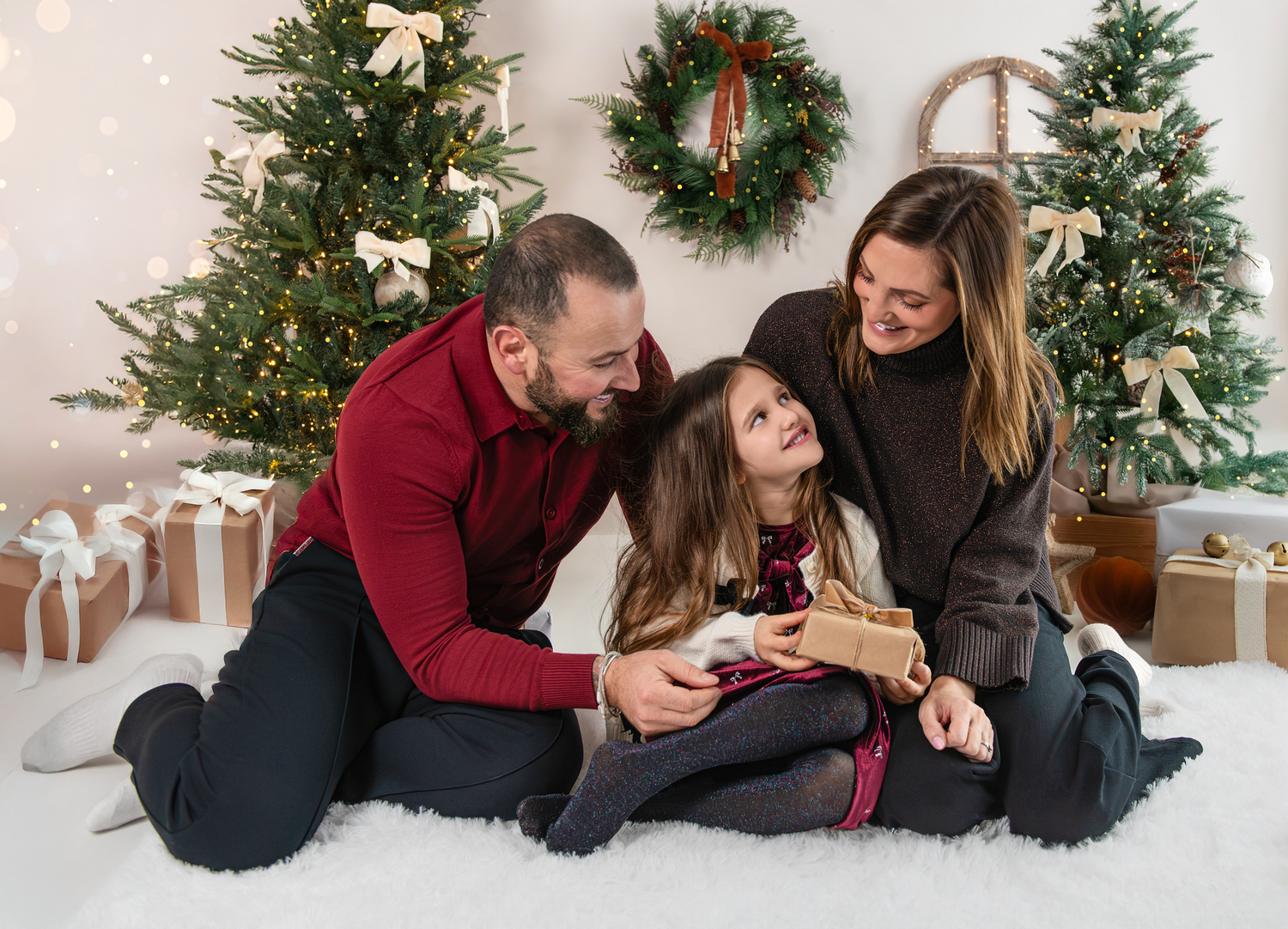 A group of people laying on a floor near Christmas trees and holiday decorations share joyful moments together.