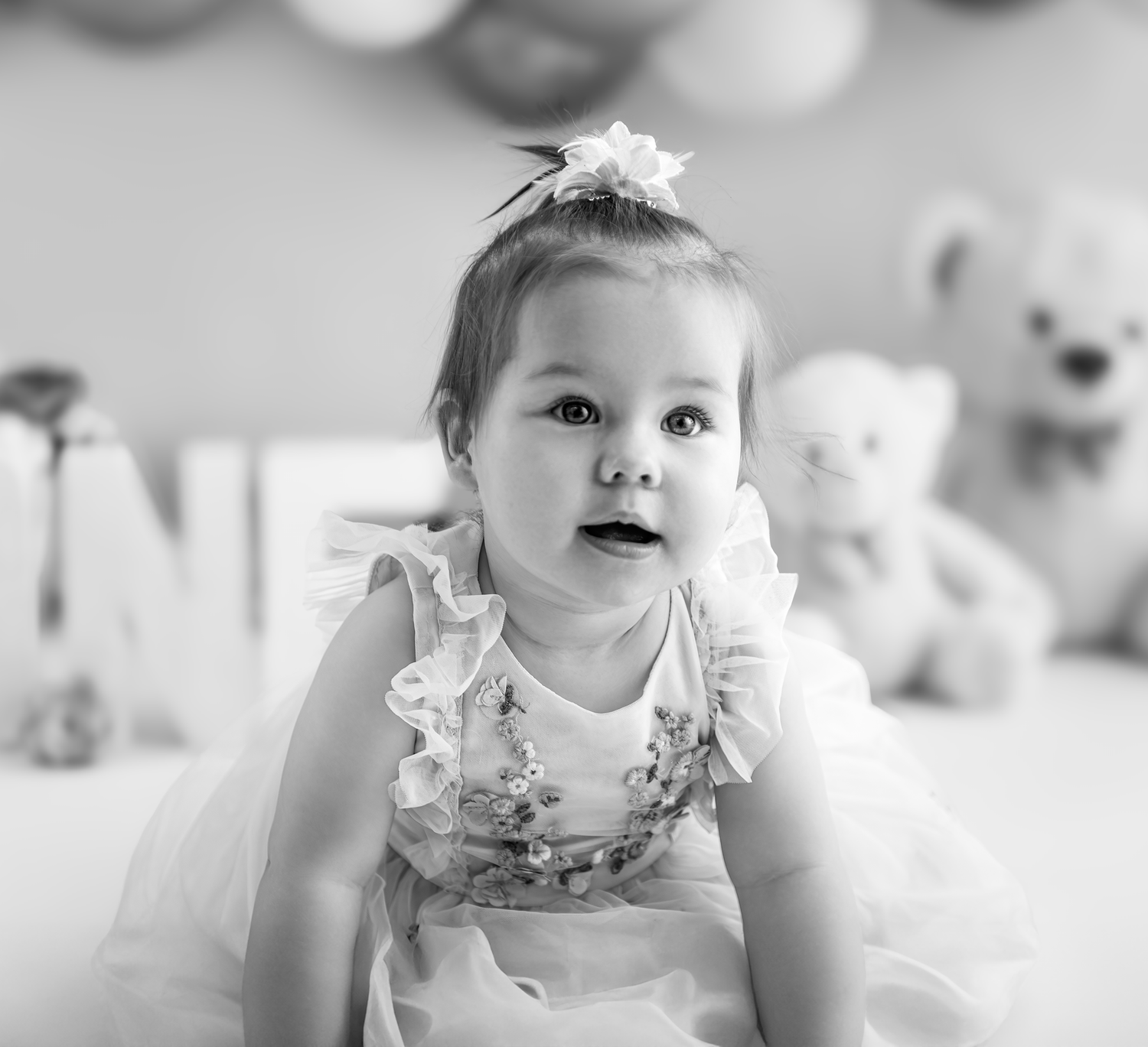 A series of black and white photos showing a baby in a floral dress sitting and posing at different angles.