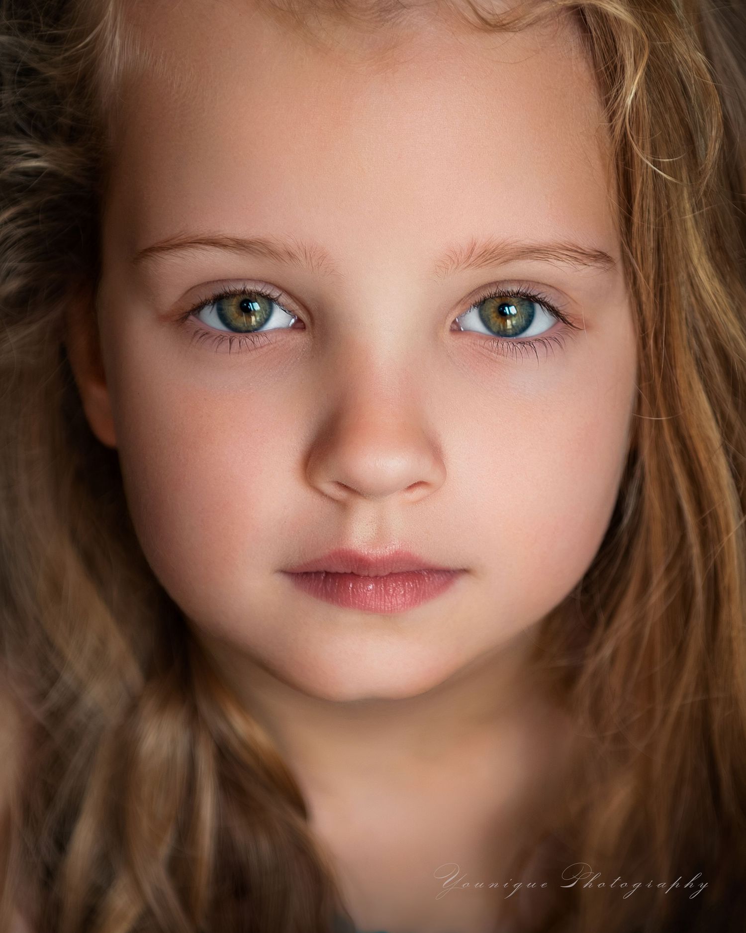 Close-up portrait of a young girl with striking green eyes and long brown hair, captured by Monique Photography.
