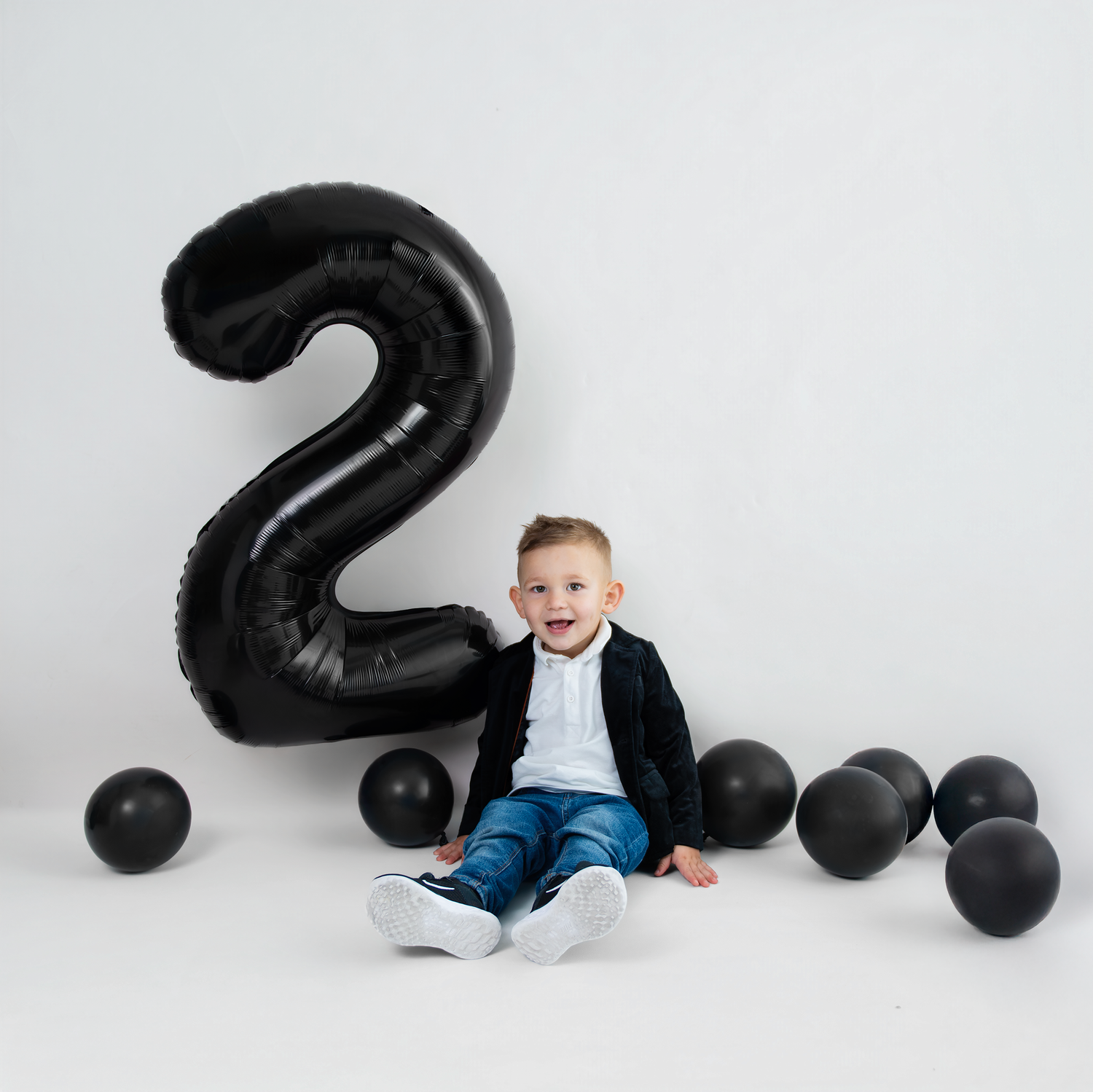 Birthday celebration setup with large black number 2 balloon and scattered black balloons against white backdrop.
