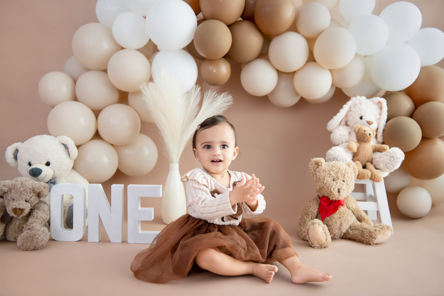A series of neutral-toned baby milestone photos with balloon decorations and teddy bear props against a beige backdrop.