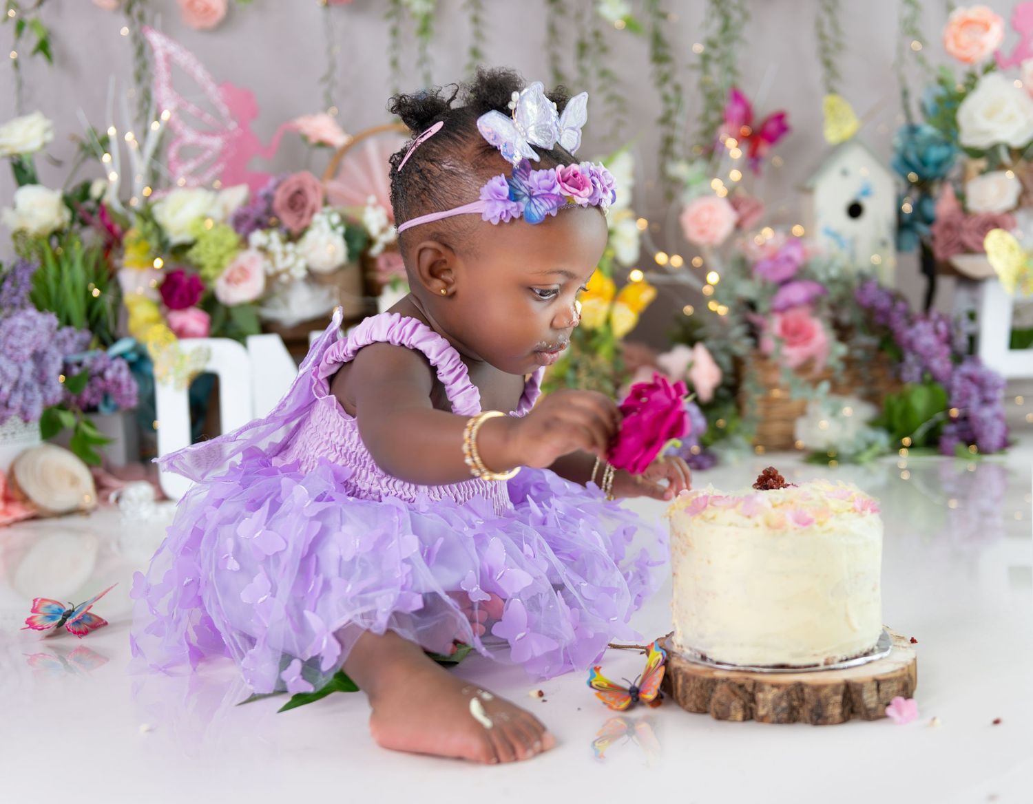 Purple tulle dress and floral backdrop create magical first birthday cake smash setting.