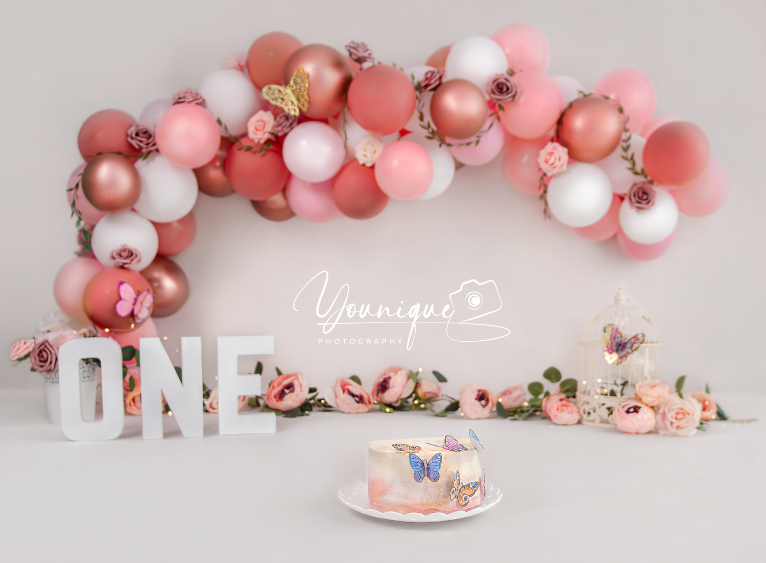 Pink and white balloon arch with floral accents decorates an elegant party setting with matching table decor.