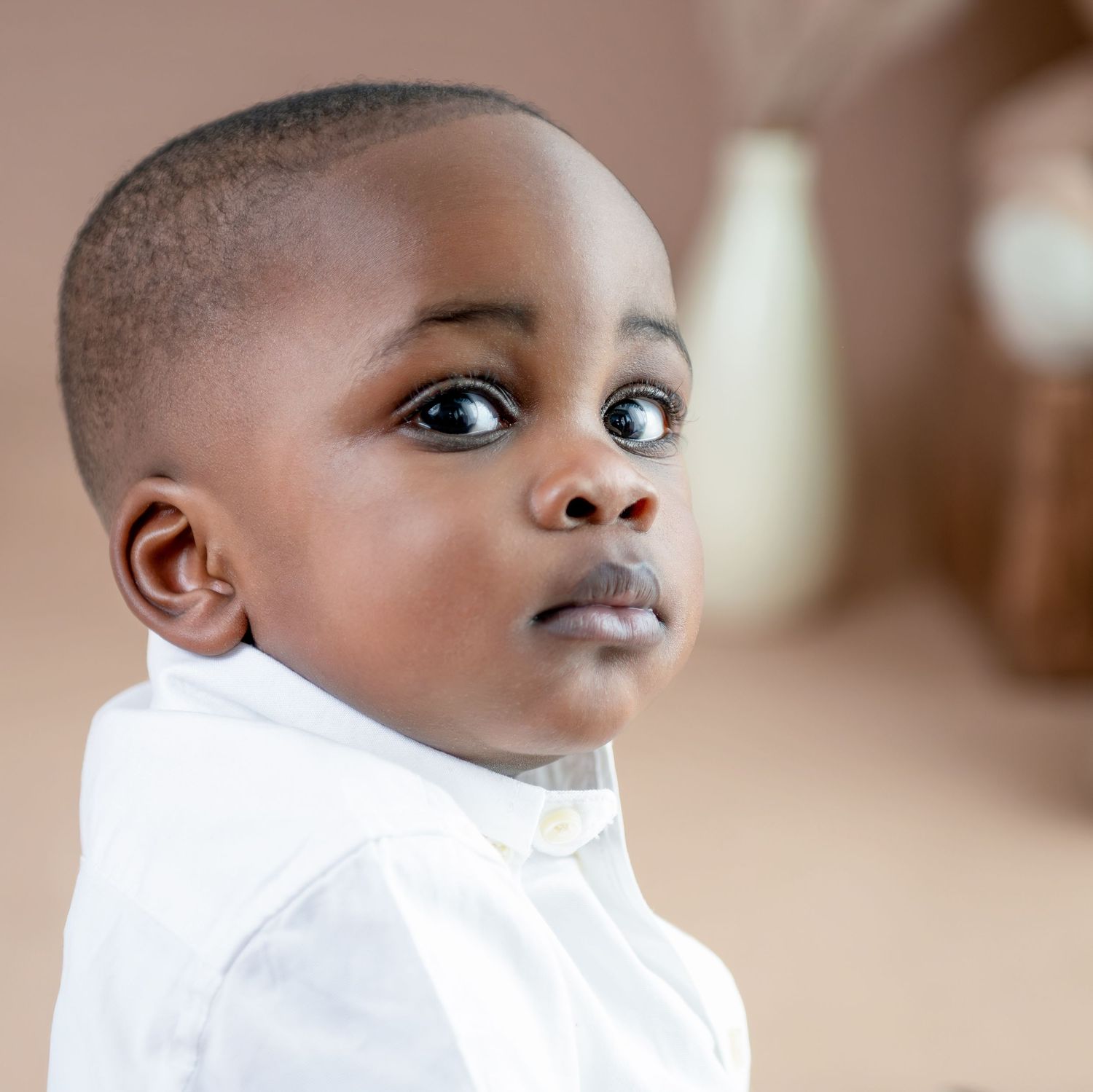 A young child in a white shirt looking to the side with a curious expression.