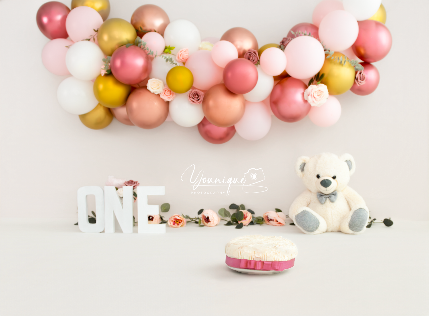 Pink and gold balloons create an elegant party backdrop with white teddy bears and floral decorations.