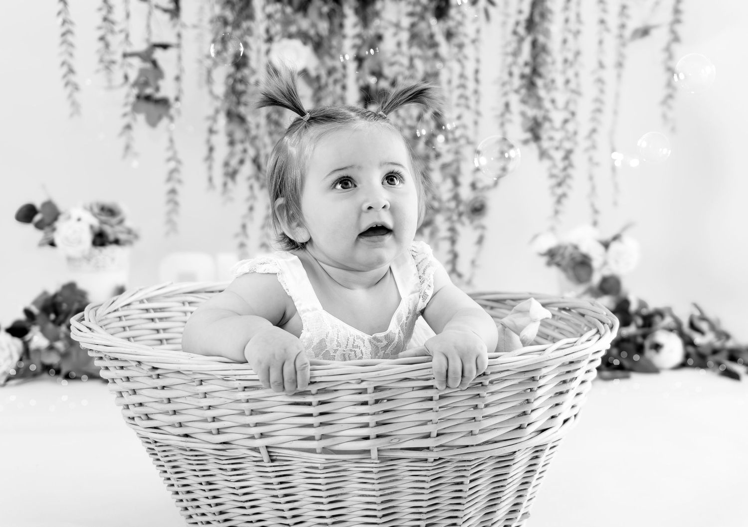 Baby sitting in white wicker basket smiling with floral backdrop.