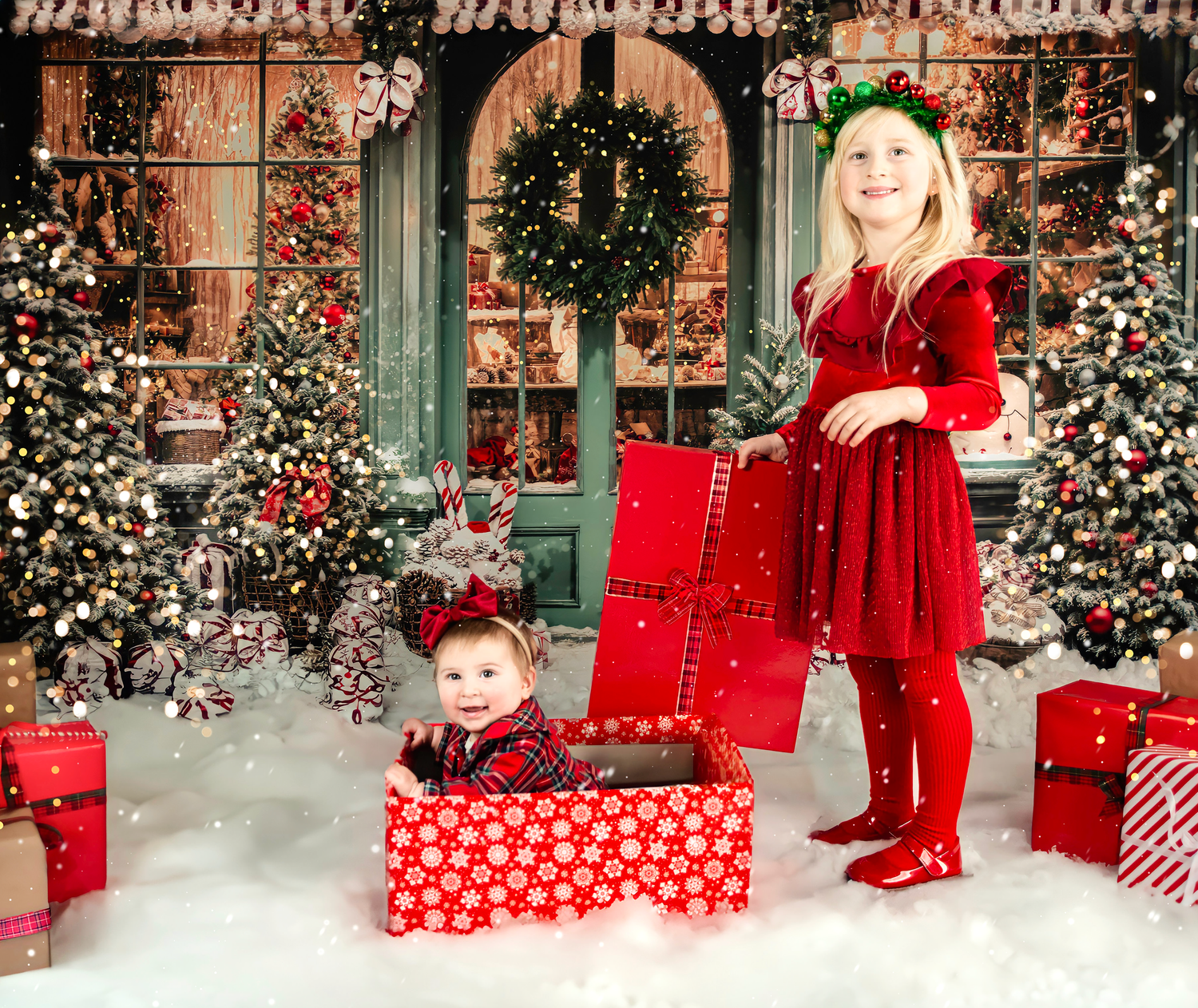Holiday photo scene with decorated Christmas trees, red wrapped presents, and snow-covered ground.