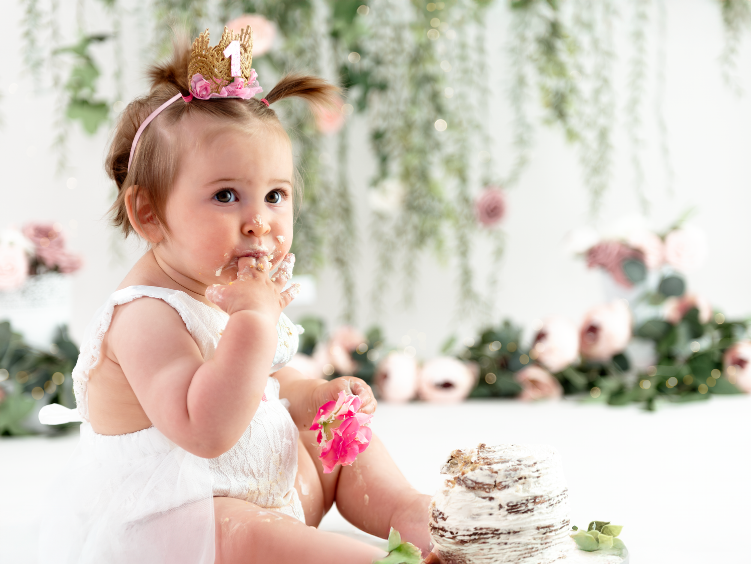 A young child in a white dress sits at an elegant garden tea party with floral decorations and pink accents.