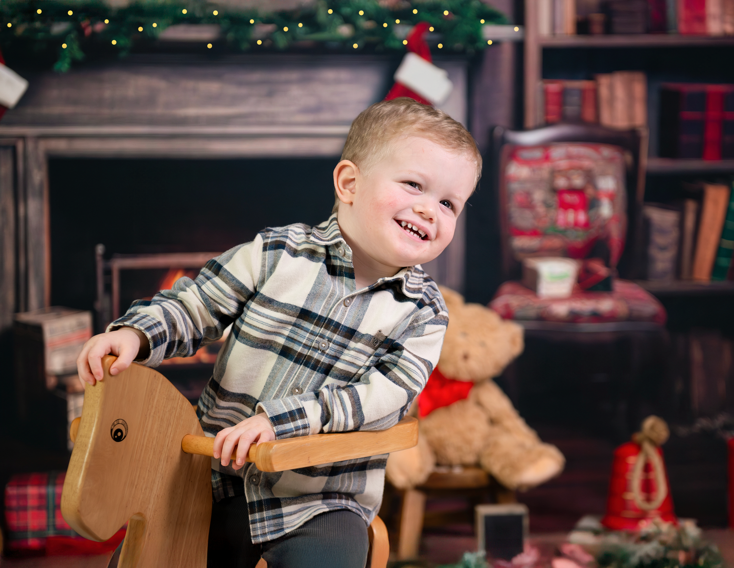 A child in a plaid shirt sits in a wooden rocking chair during Christmas time with a bookshelf in the background.