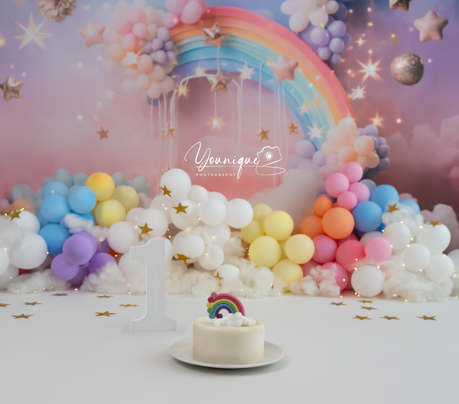 Pastel balloon arch with rainbow cake decoration against dreamy pink background with gold stars and floating clouds.