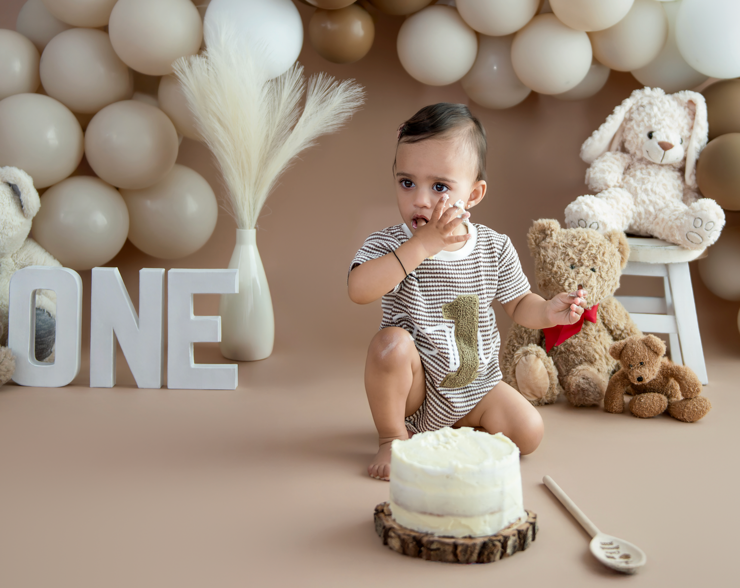 First birthday cake smash photo setup with white balloons, teddy bears, and 