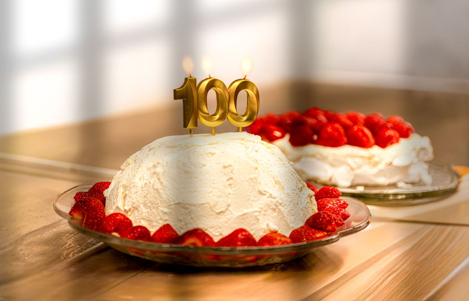 White frosted cake with red strawberries displayed on wooden table in natural lighting.