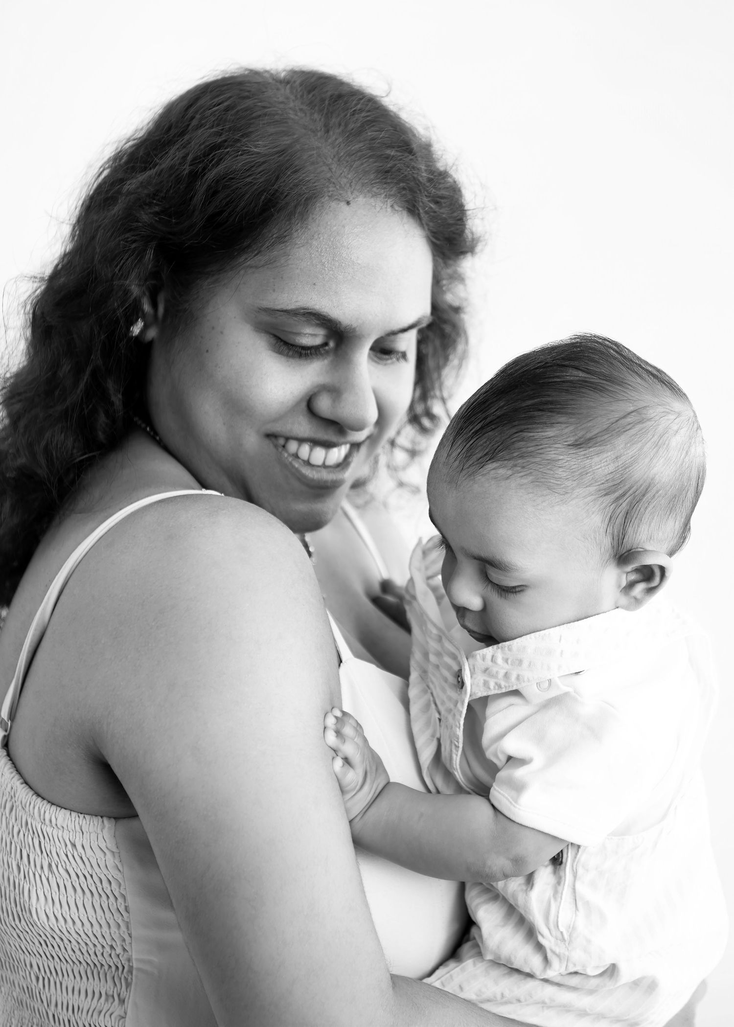 Black and white photo of a smiling mother holding her sleeping baby, sharing a tender moment together.