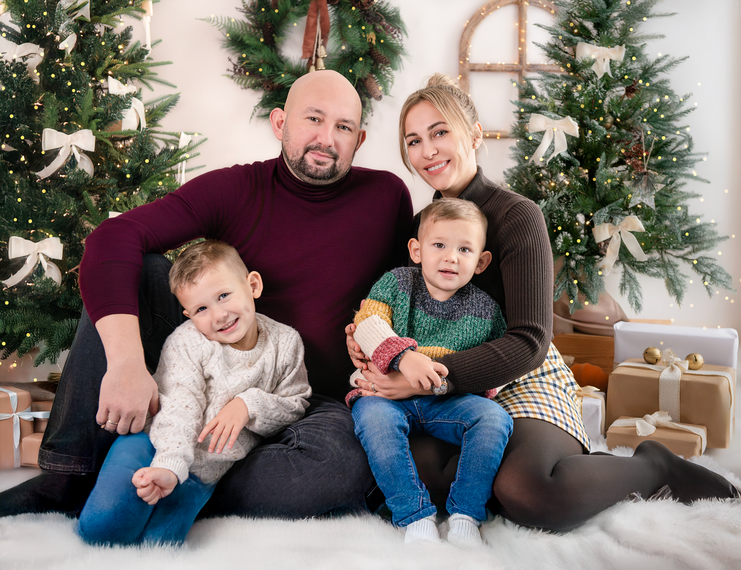 A family poses together for a holiday portrait in front of decorated Christmas trees and wreaths.