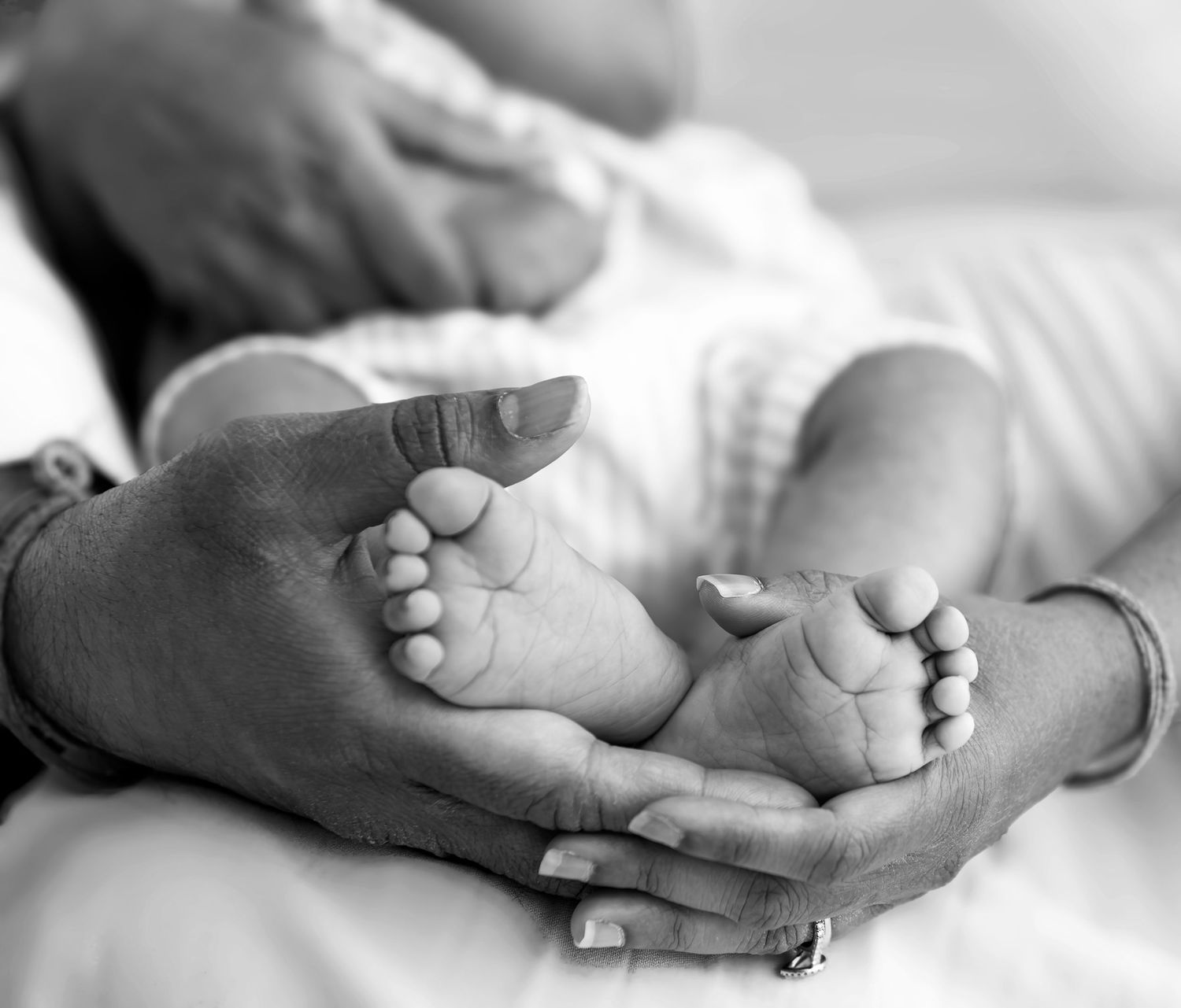 Black and white photo of a newborn baby's tiny feet cradled gently in loving adult hands.