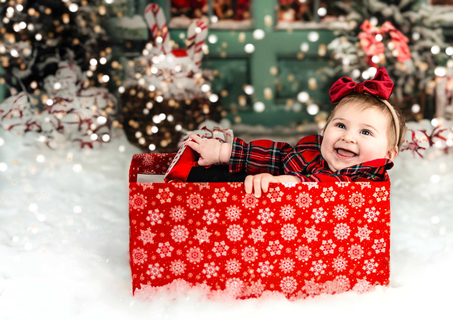 Red and white presents with plaid ribbon lie scattered under a snowy Christmas tree with twinkling lights.