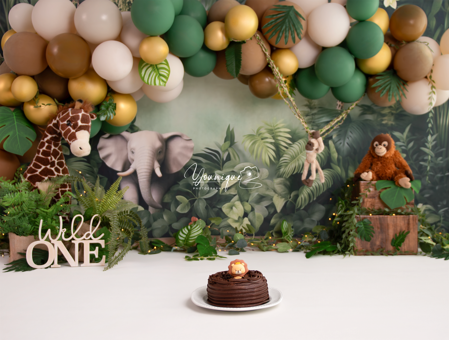 Wild One jungle themed first birthday cake smash setup with balloon arch, safari animals, and chocolate smash cake.