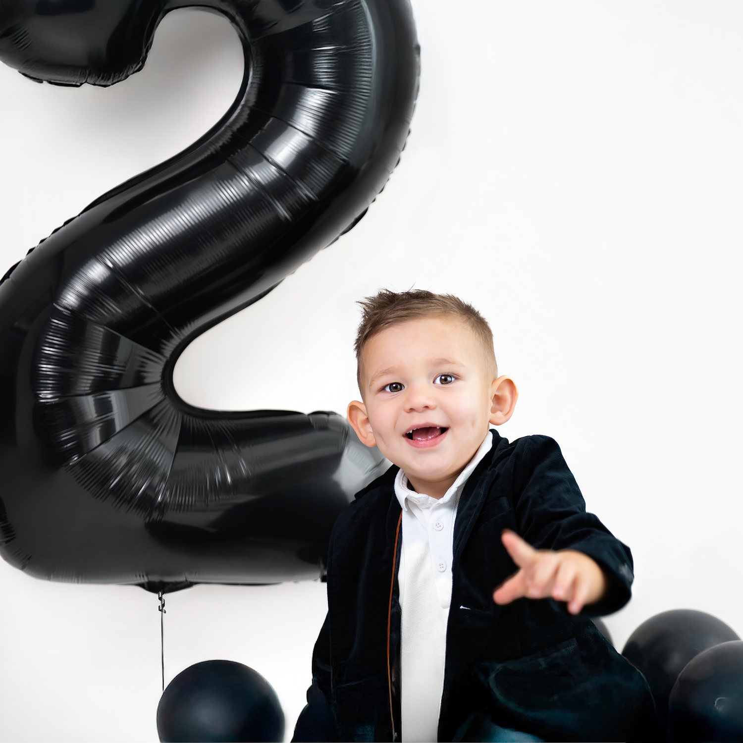 Black number balloons and formal attire create a stylish birthday photo session against a white backdrop.