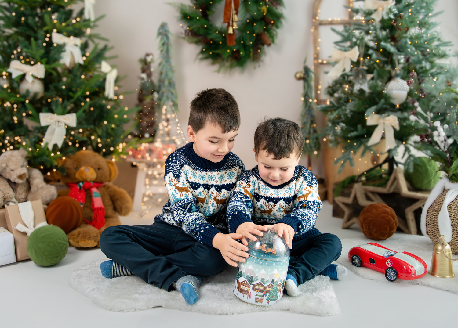 Children in matching holiday sweaters sit together with Christmas decorations and toys in a festive setting.