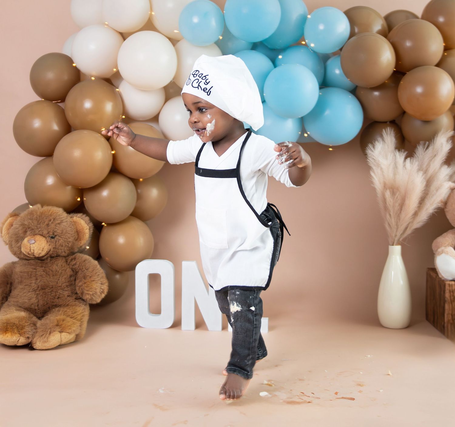 Festive balloon arch display in brown and blue tones with pampas grass decorations and teddy bear accents for a celebration.