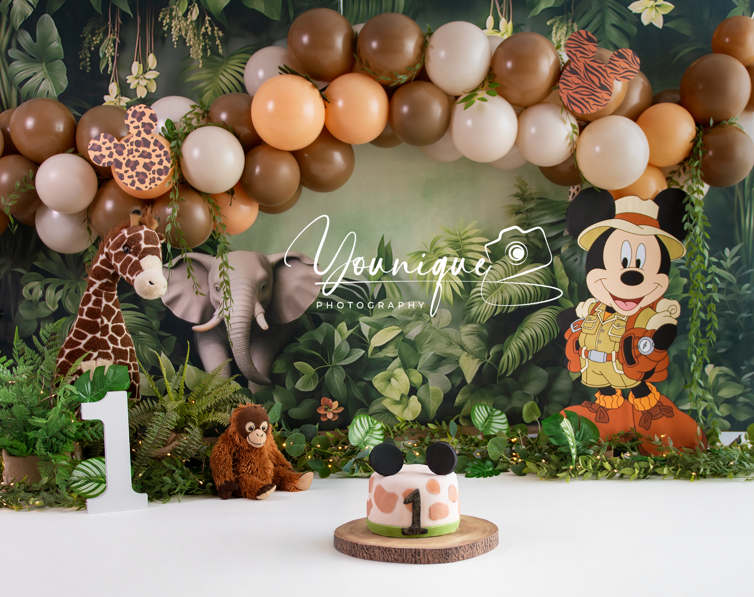 Safari-themed first birthday party setup with Mickey Mouse decor, balloon arch, and jungle greenery backdrop.