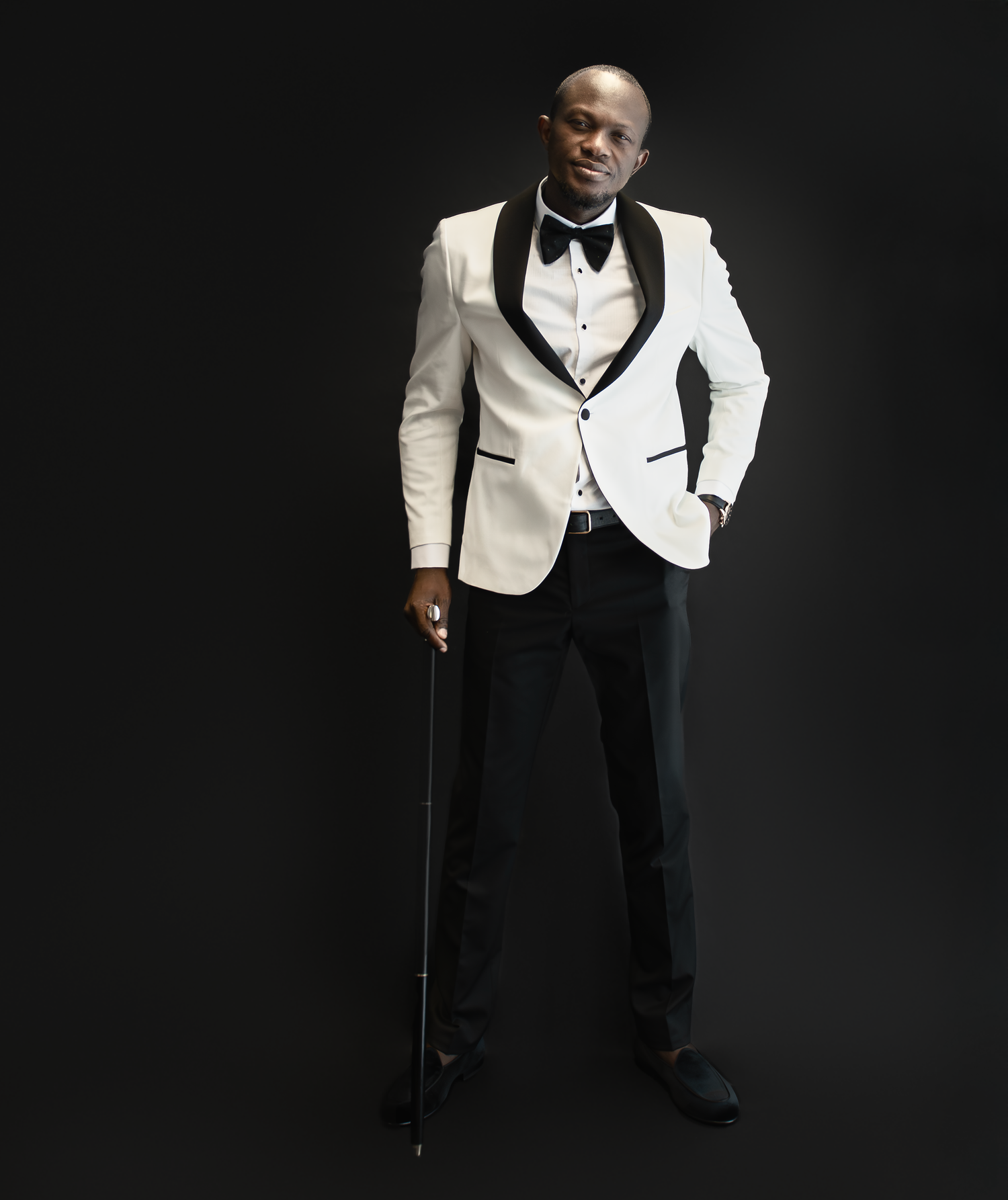 Elegant figure in white tuxedo jacket and bow tie against dark background.