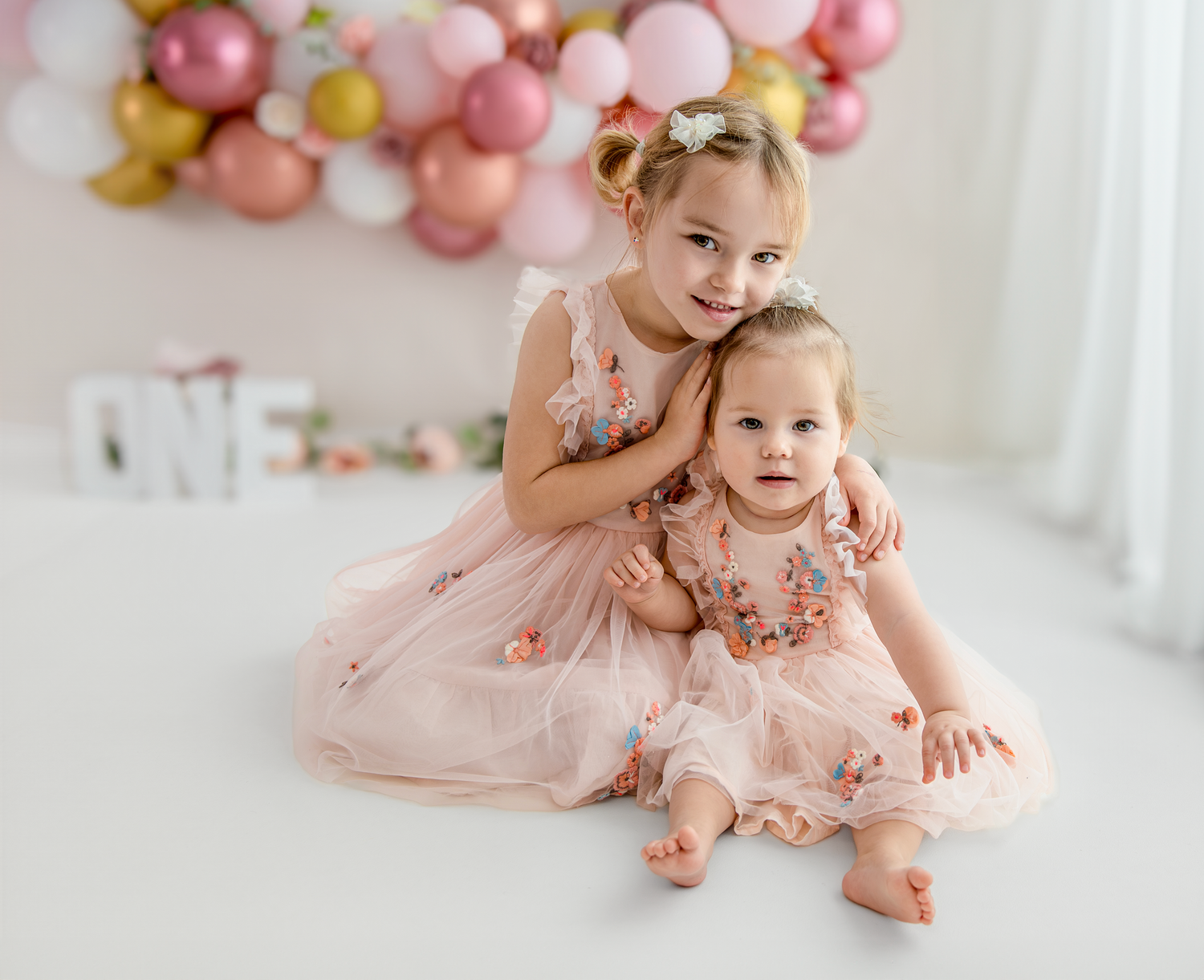 A series of pink balloon decorations and tulle dresses create a soft and dreamy photo session setting.
