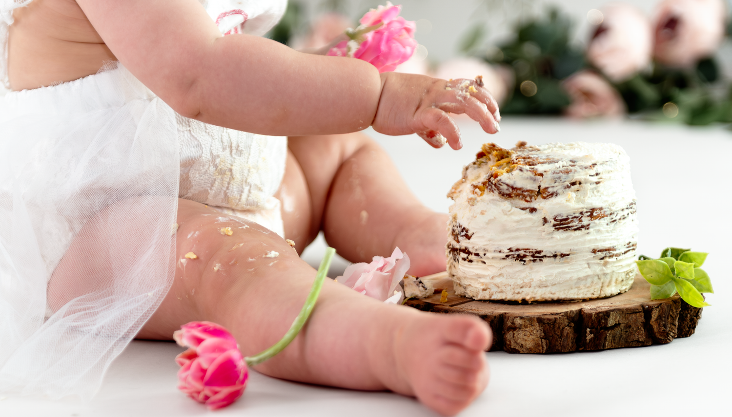 Small baby feet next to a pink flower and decorative cake on a white surface.