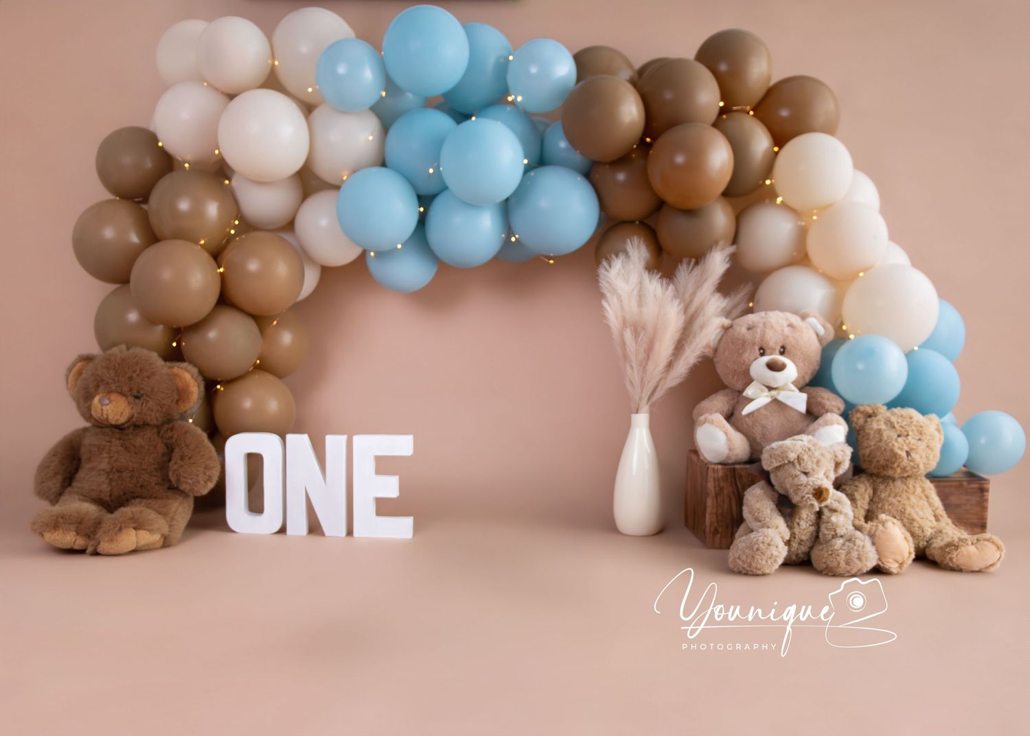 A collage showing progression of blue and white balloon garland installation with teddy bears and 'ONE' text decoration.