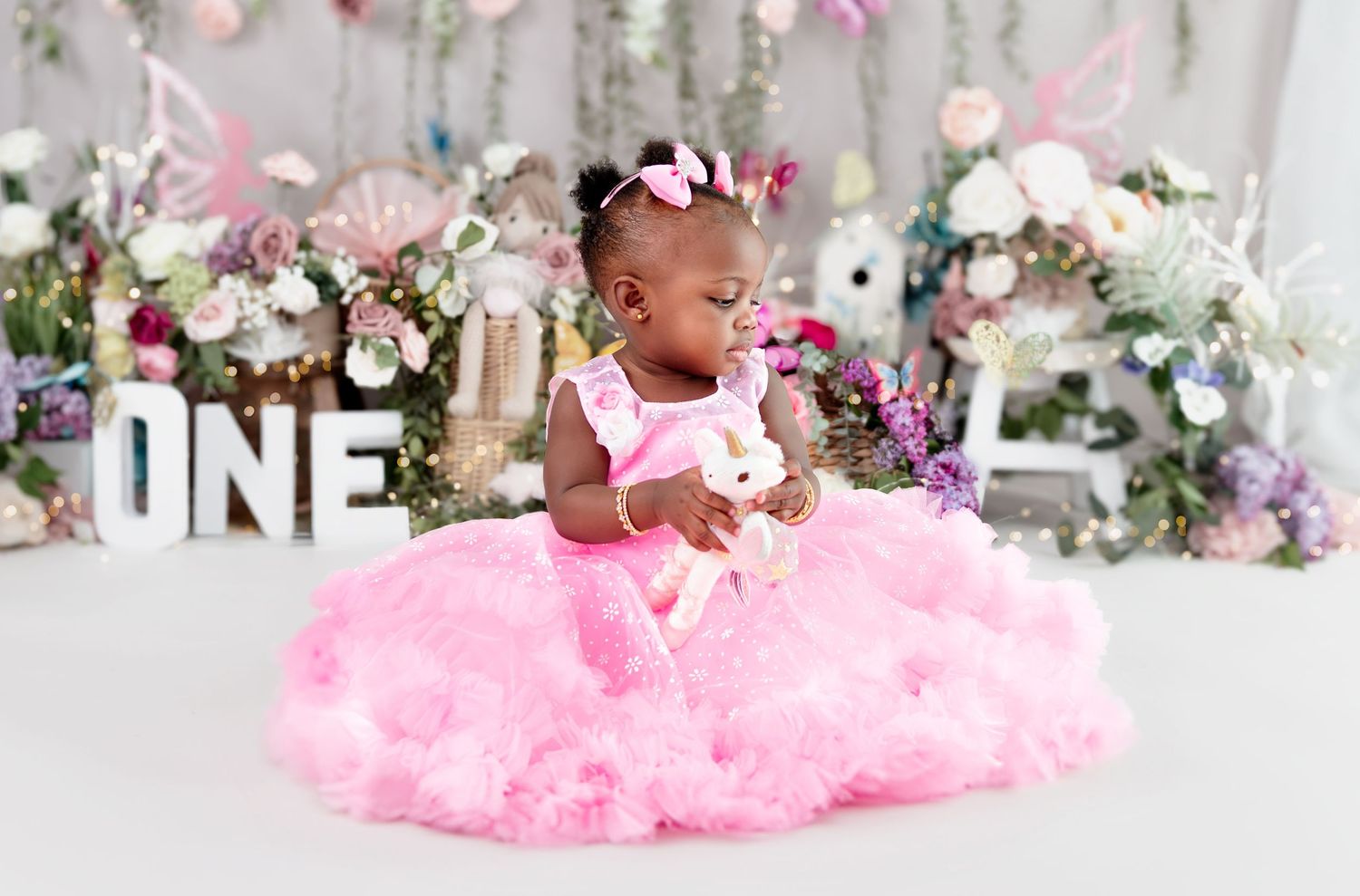 Decorated birthday scene with pink tulle, floral garlands, and 'ONE' letter sign.