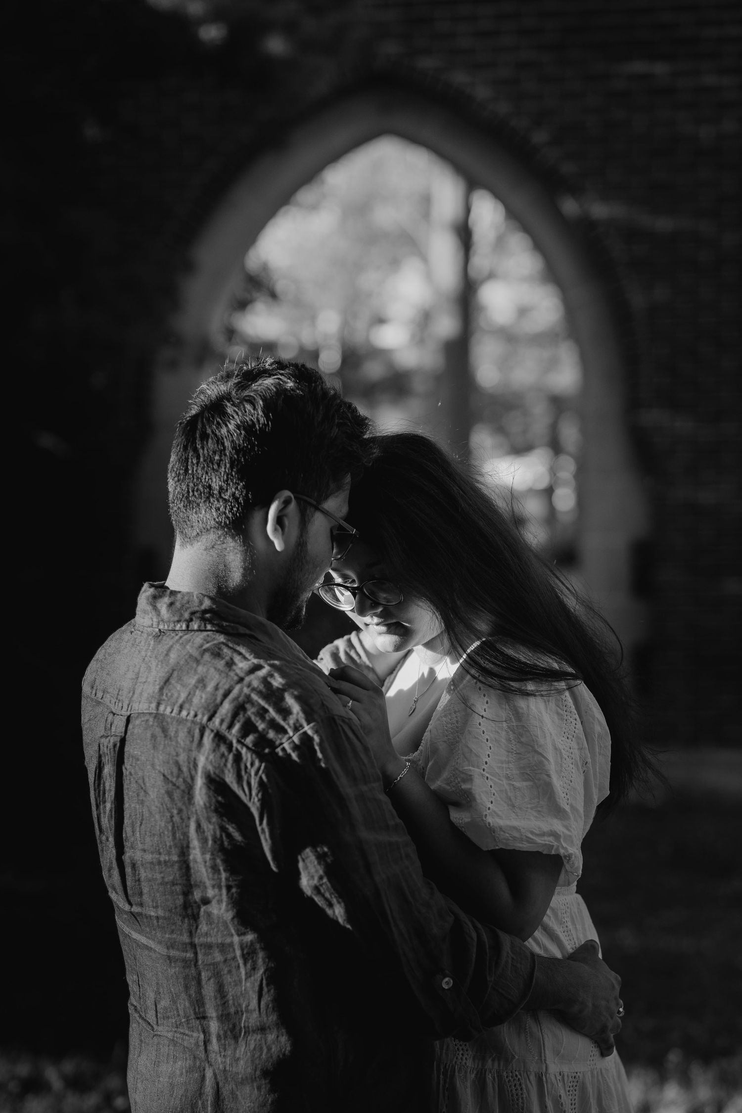 Black and white photo of couple touching foreheads near arched stone window
