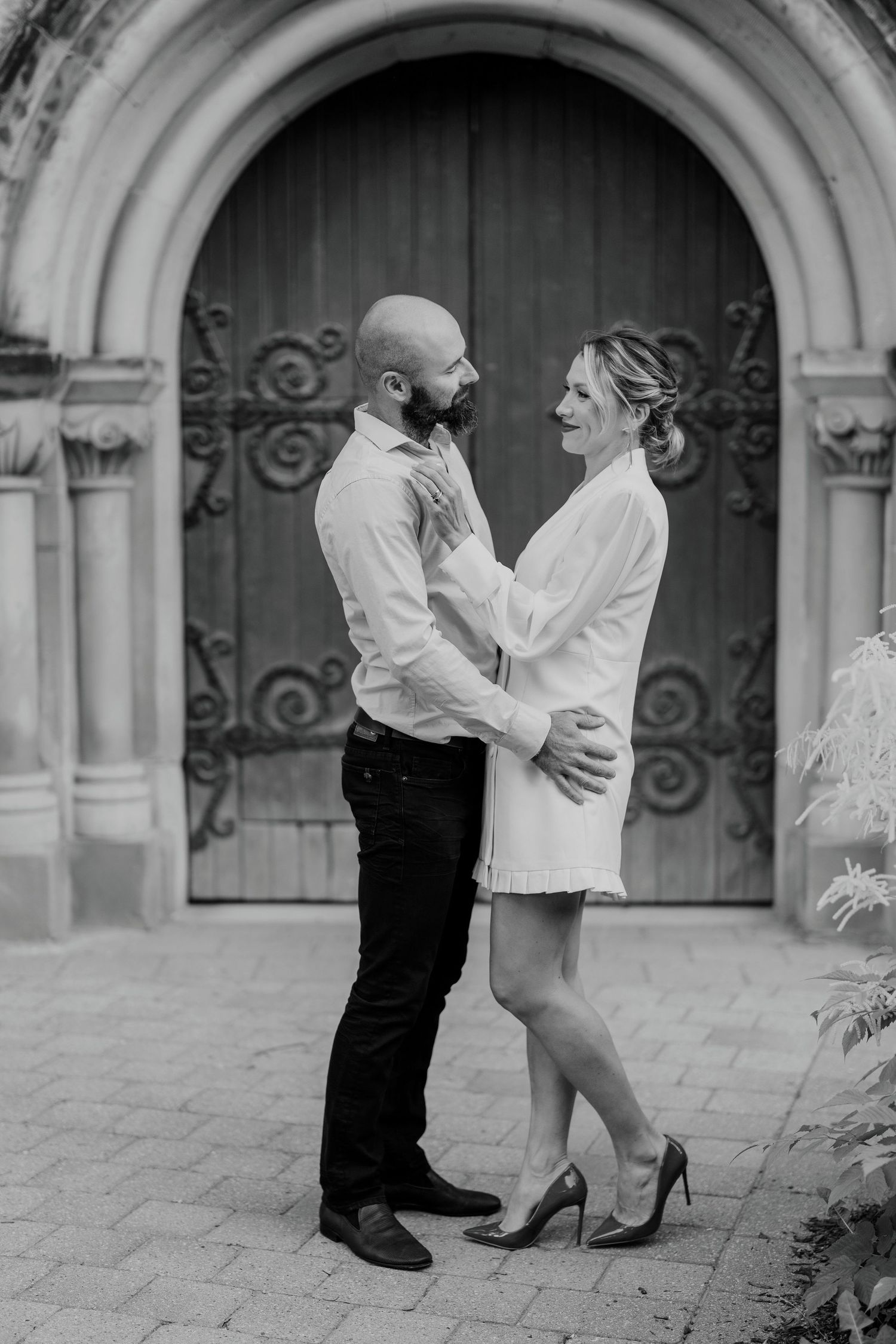 Playful engagement moment of couple dancing in front of gothic stone doorway