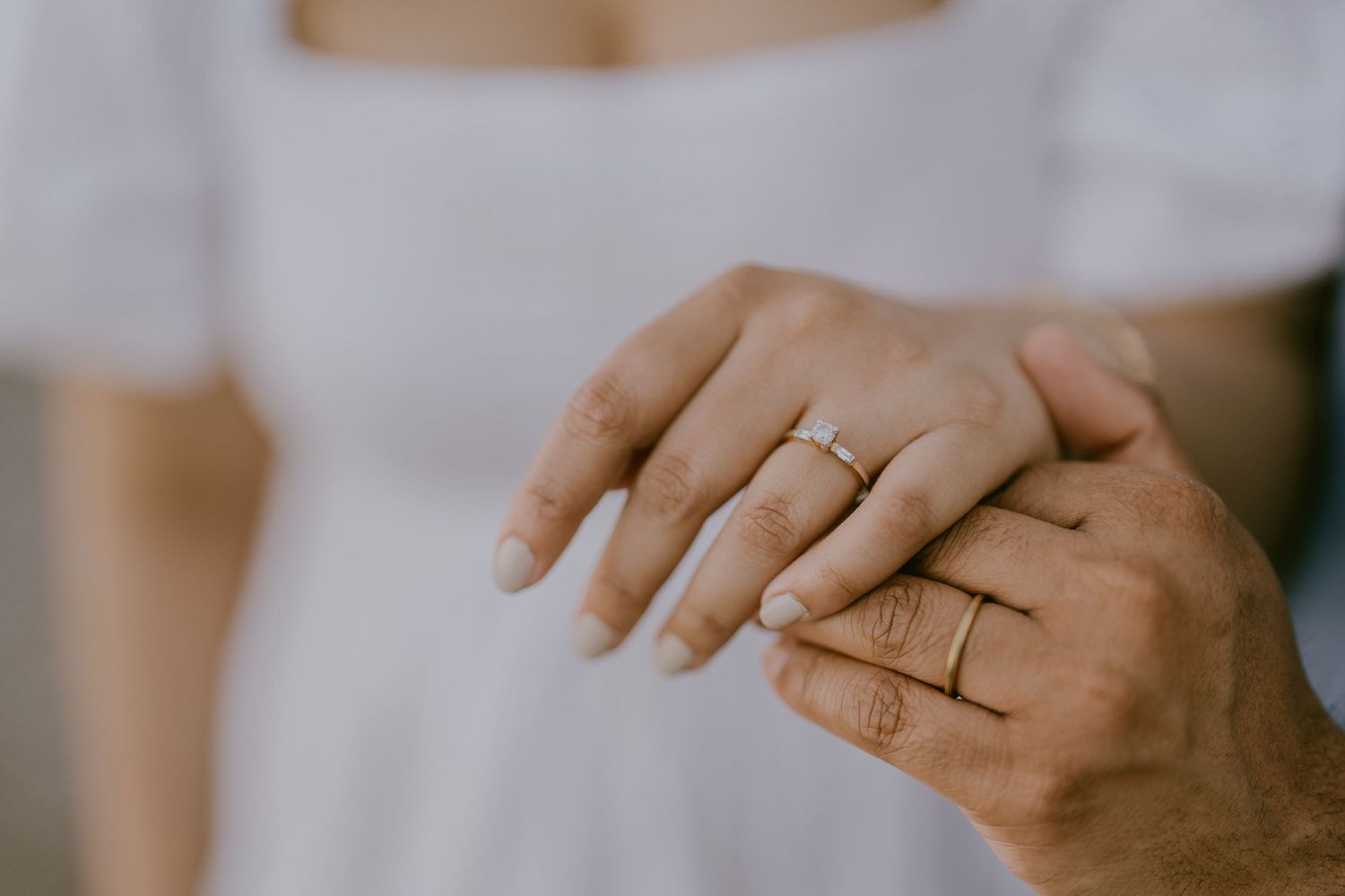 Close-up of couple holding hands showing engagement rings