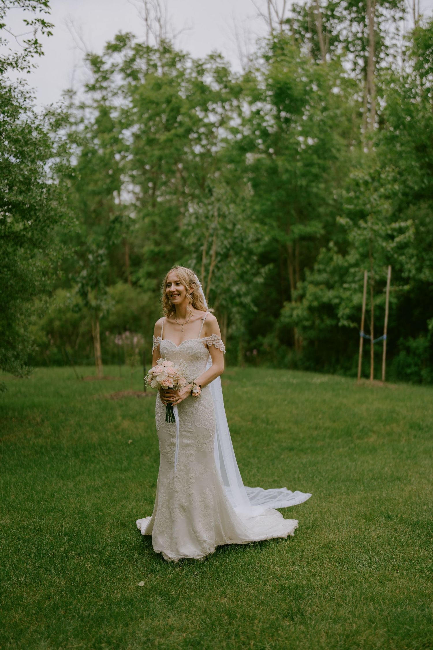 Bride standing in open field with bouquet and soft smile