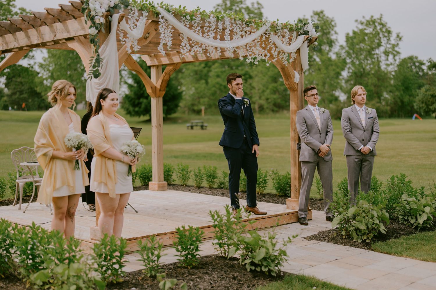 Groom and groomsmen waiting under rustic outdoor arbor before wedding ceremony