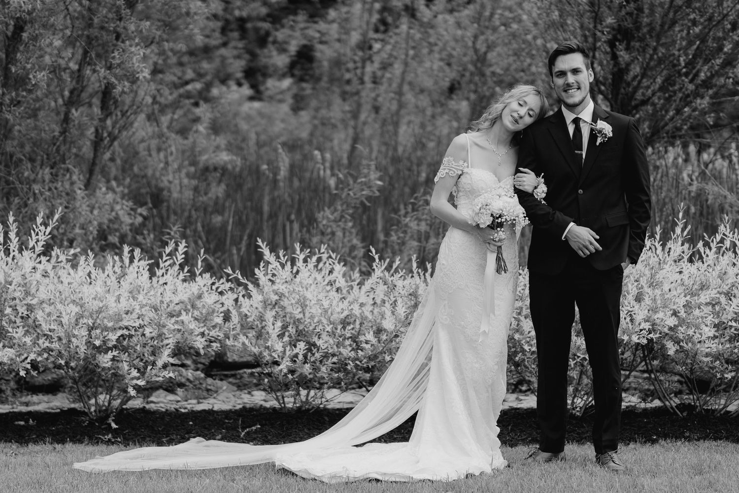 Split-tone portrait of bride and groom in garden with long dress train