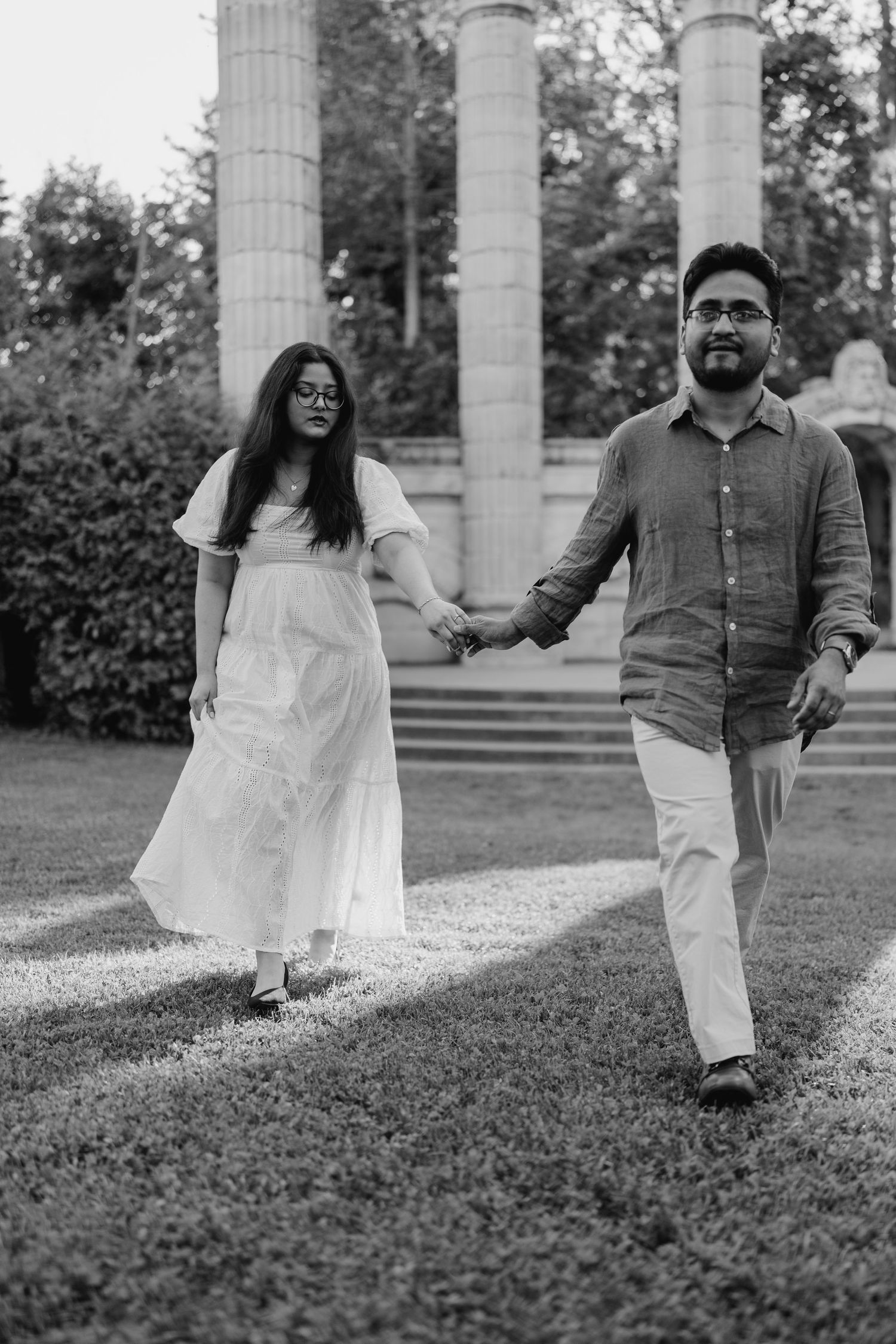 Black and white engagement photo of couple walking together past stone columns