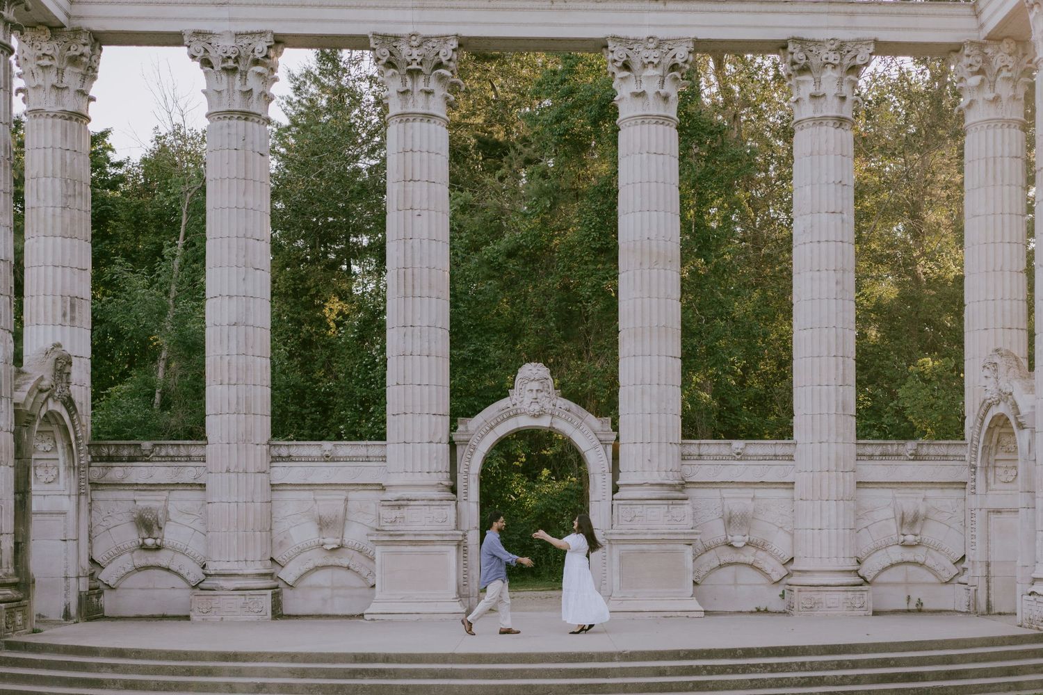 Cinematic photo of couple walking hand-in-hand in front of grand colonnade