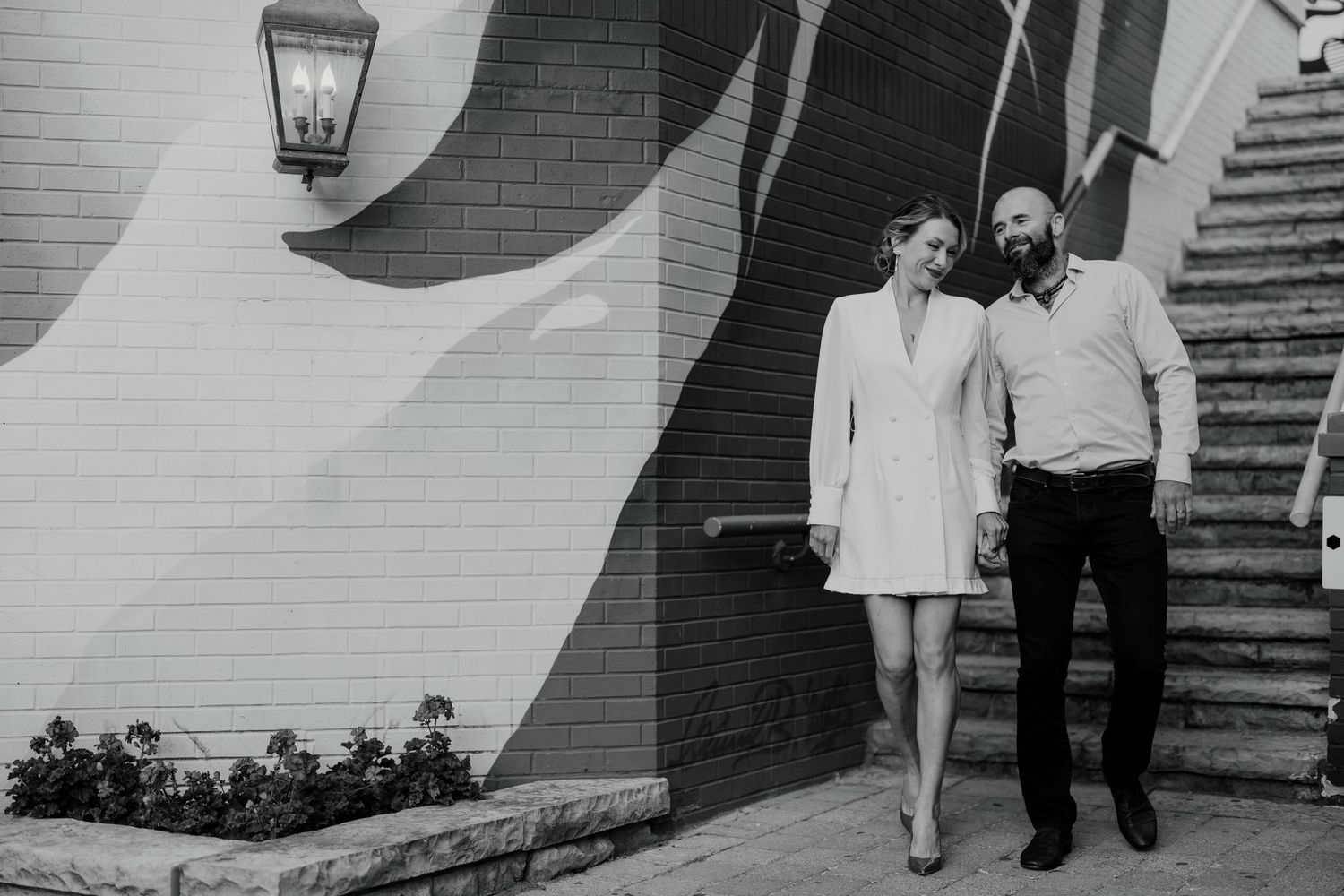 Black and white image of wedding couple walking hand-in-hand by mural-covered wall and steps
