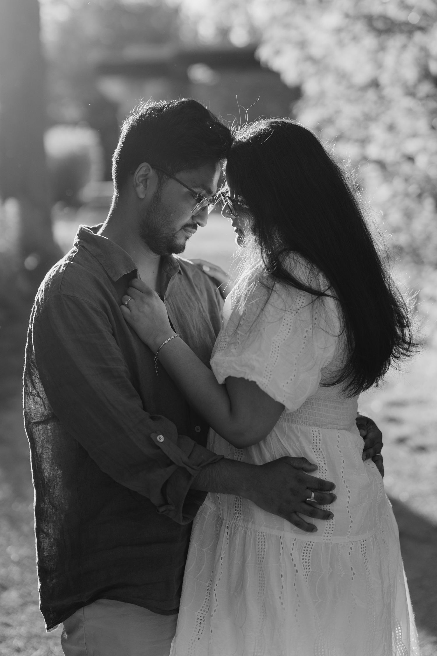 Black and white photo of couple embracing in sun-dappled forest