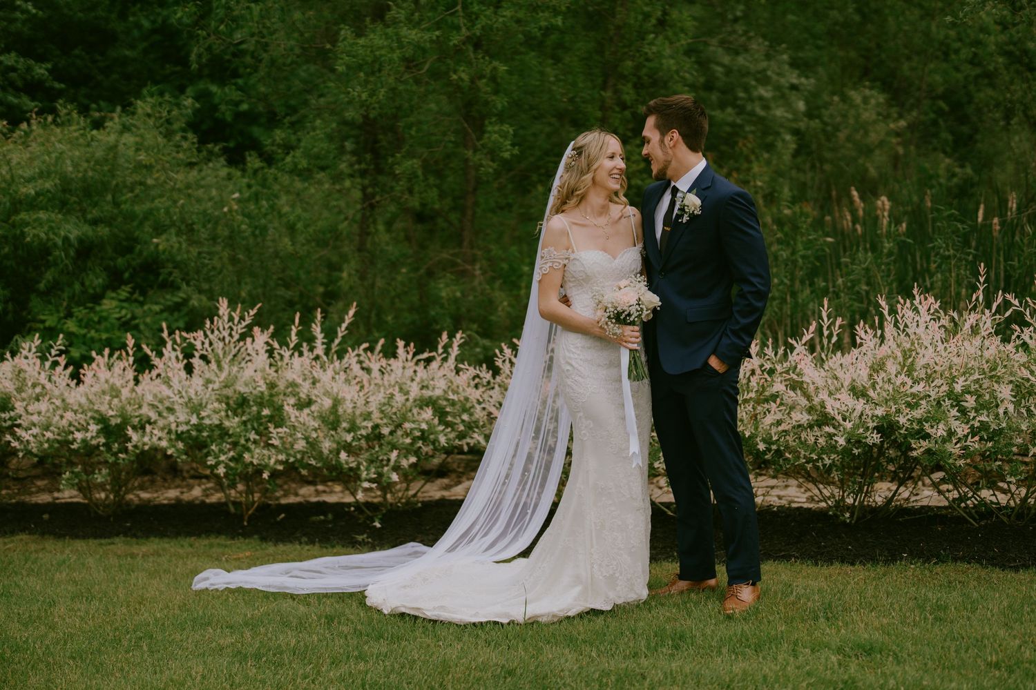 Elegant wedding portrait of bride and groom walking together across a garden lawn  in Oshawa, Ontario
