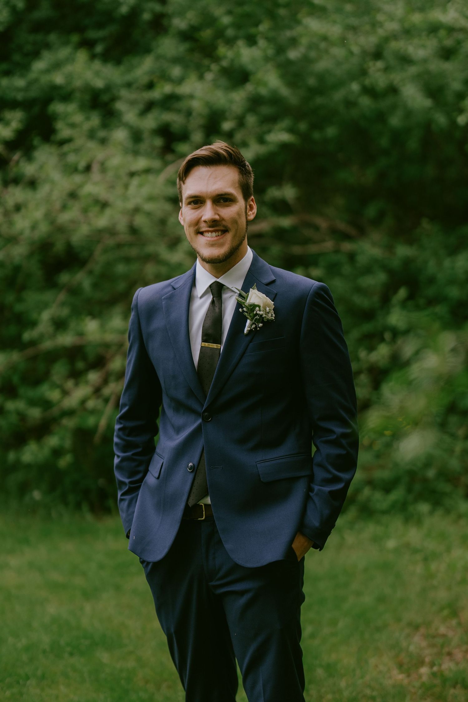 Groom in navy suit standing on green lawn with soft smile