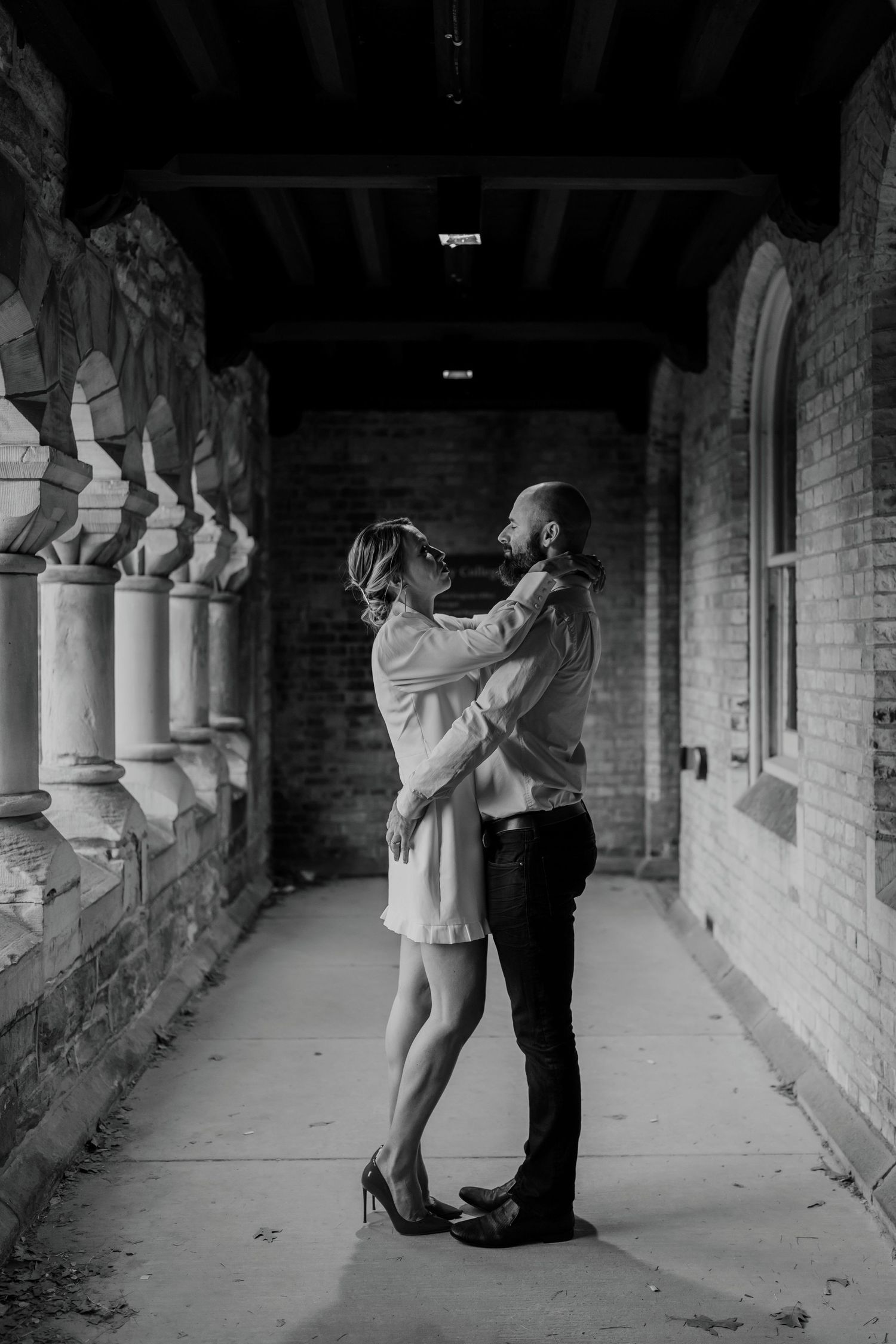 Artistic black and white portrait of couple embracing in gothic stone corridor