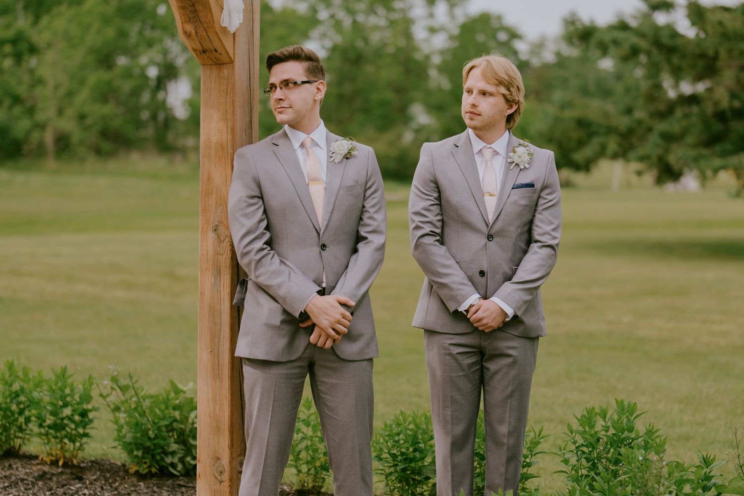Two groomsmen standing in grey suits during outdoor ceremony