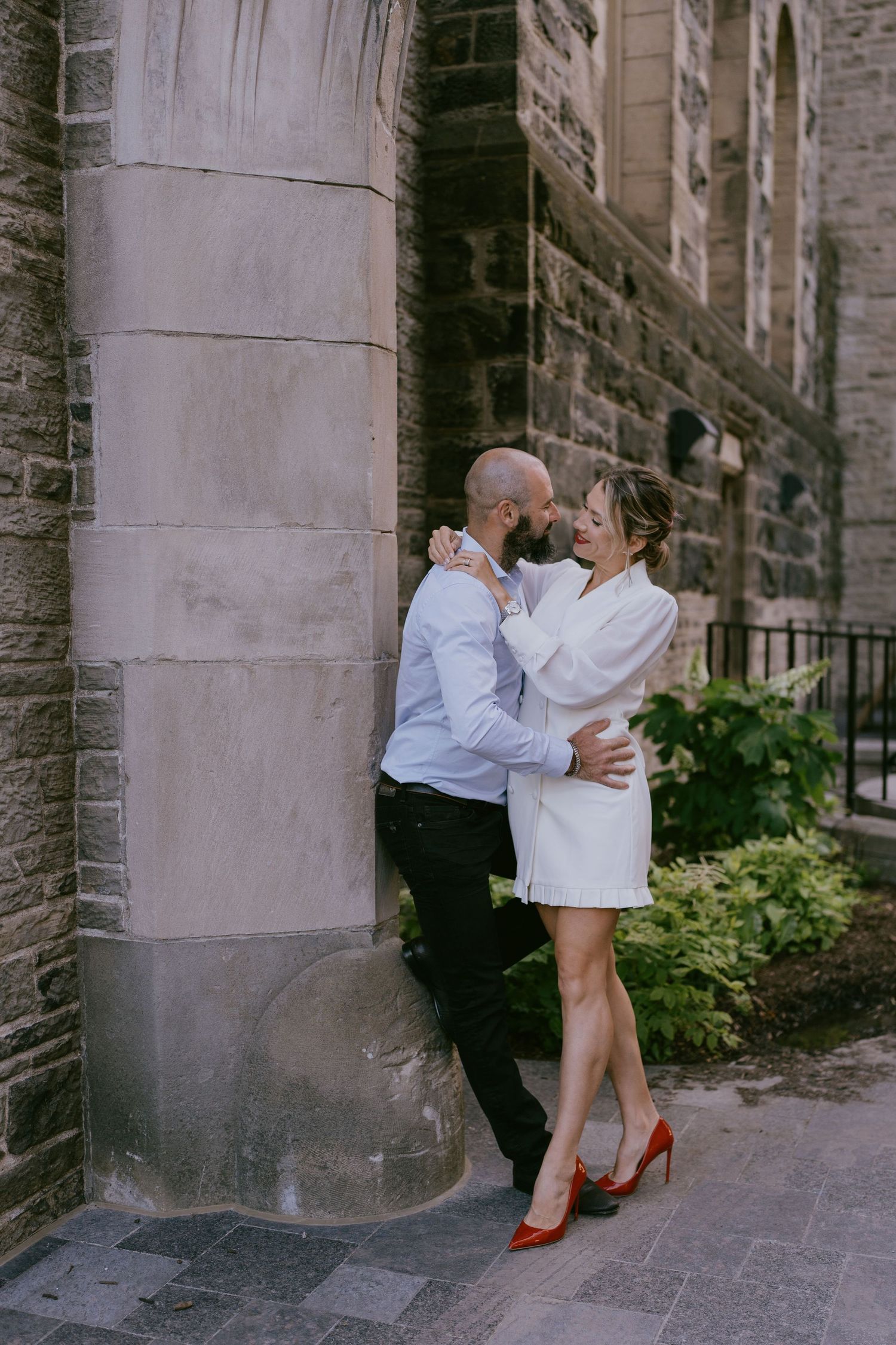 Cozy engagement photo of couple snuggled up beside a stone building column
