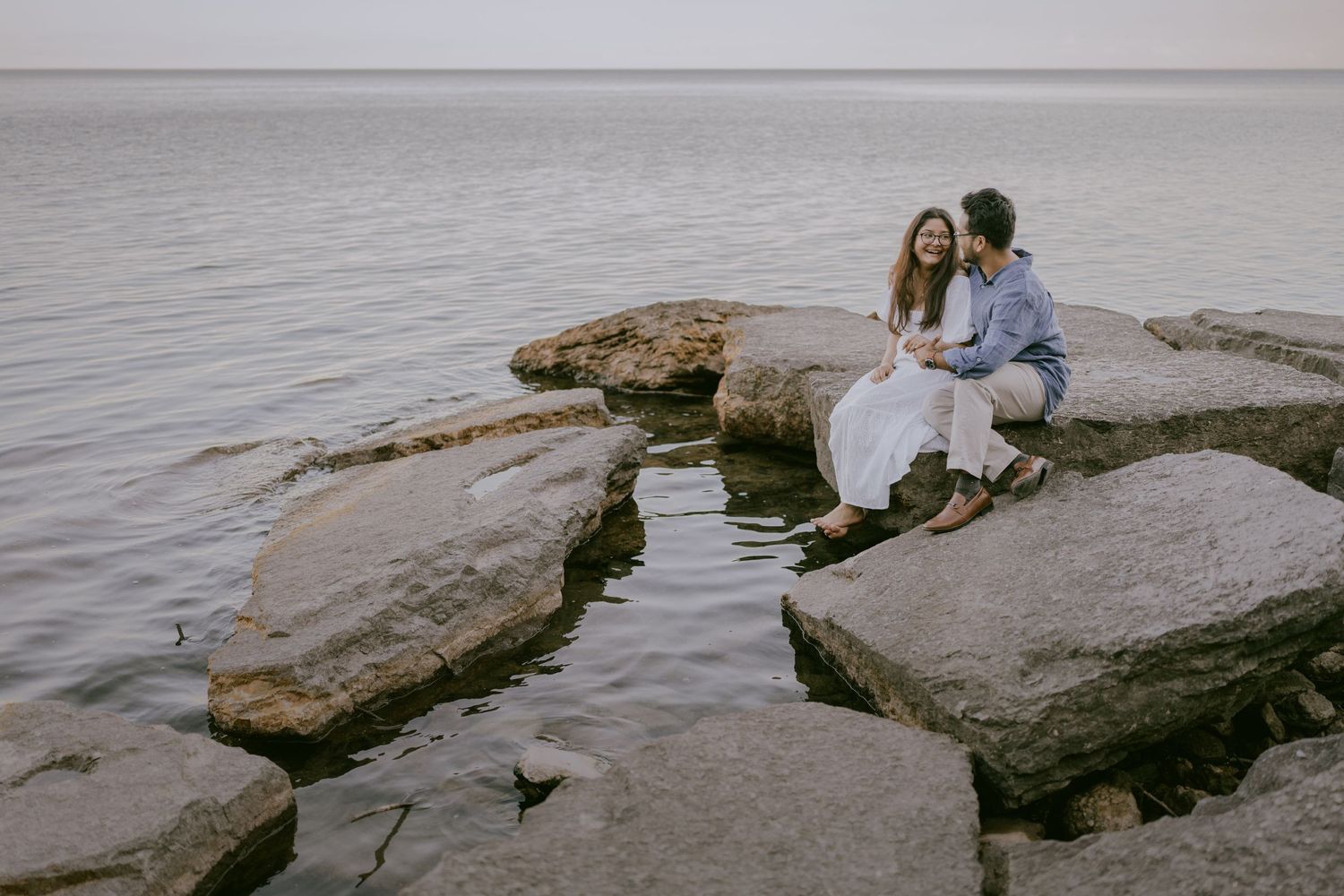 Smiling couple sitting on shoreline rocks with lake in the background